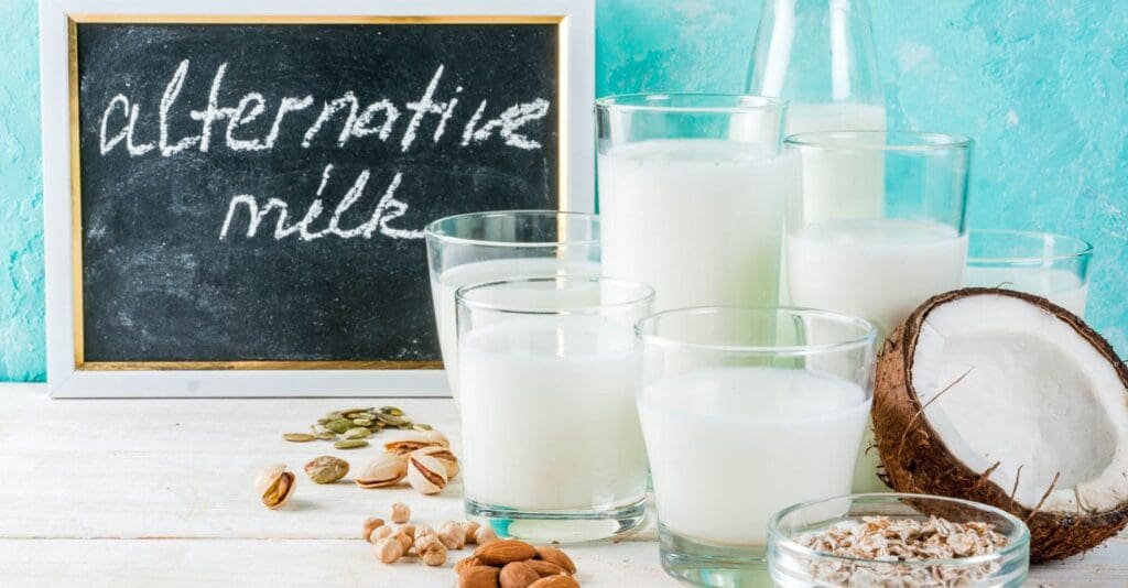 Tavolo bianco con sopra vari bicchieri di latte vegetale e lavagna con la scritta "alternative milk"