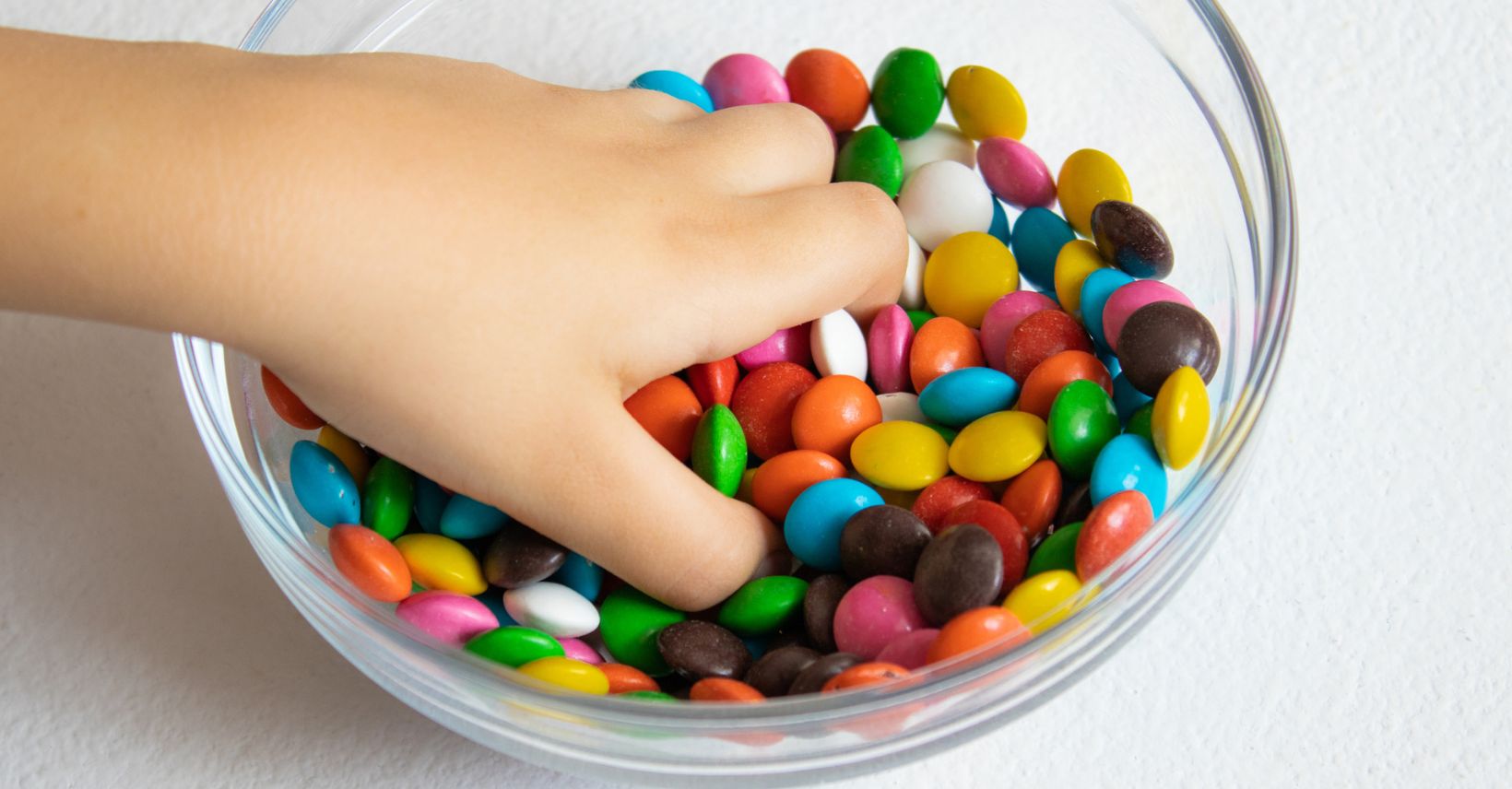 Mano di bambino che prende caramelle da una ciotola di vetro